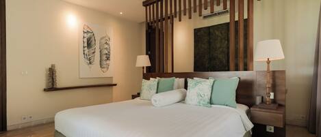 A spacious bedroom with a large bed, wooden headboard, two bedside tables with lamps, a ceiling fan, and artwork on the walls.