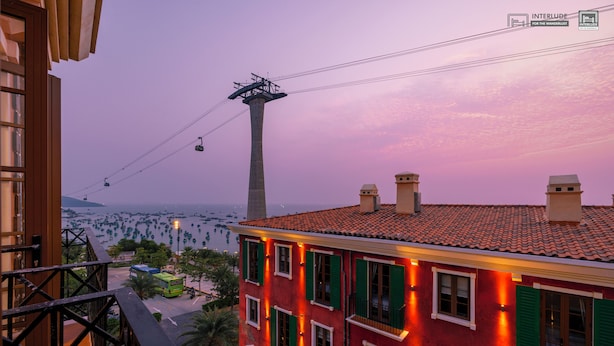 A red building with green shutters and a balcony overlooking a street with buses and a tall tower. - MARCO'S INTERLUDE Hotel Phu Quoc (Phu Quoc)