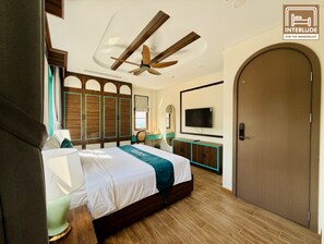 A hotel room with a bed, a ceiling fan, a TV, a wardrobe, and a door. - MARCO'S INTERLUDE Hotel Phu Quoc (Phu Quoc)