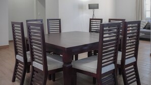 A dining area with a rectangular table surrounded by six wooden chairs with slatted backs and cushioned seats. The room has a tiled floor, white walls, and recessed ceiling lighting. - Modern Flat with 2 Bedrooms Near sea (Ciudad Madero)