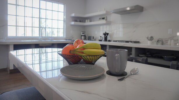 A kitchen with a marble countertop, a bowl of fruit, a mug, and a spoon. - Modern Flat with 2 Bedrooms Near sea (Ciudad Madero)