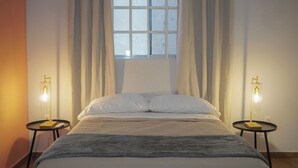 A bedroom with a bed, two bedside tables with lamps, a window with curtains, and an air conditioning unit on the wall. - Modern Flat with 2 Bedrooms Near sea (Ciudad Madero)