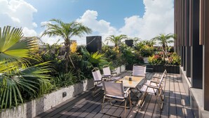 Een terras buiten met een houten tafel en stoelen, omgeven door weelderige begroeiing en palmbomen.