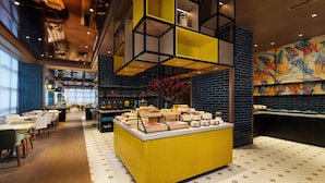 Een modern restaurant met een centraal buffet, hoge plafonds en een levendige muurschildering.