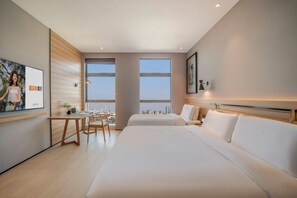 Une chambre d’hôtel moderne avec un grand lit, un bureau et une chaise. Deux fenêtres offrent une vue sur le paysage urbain.