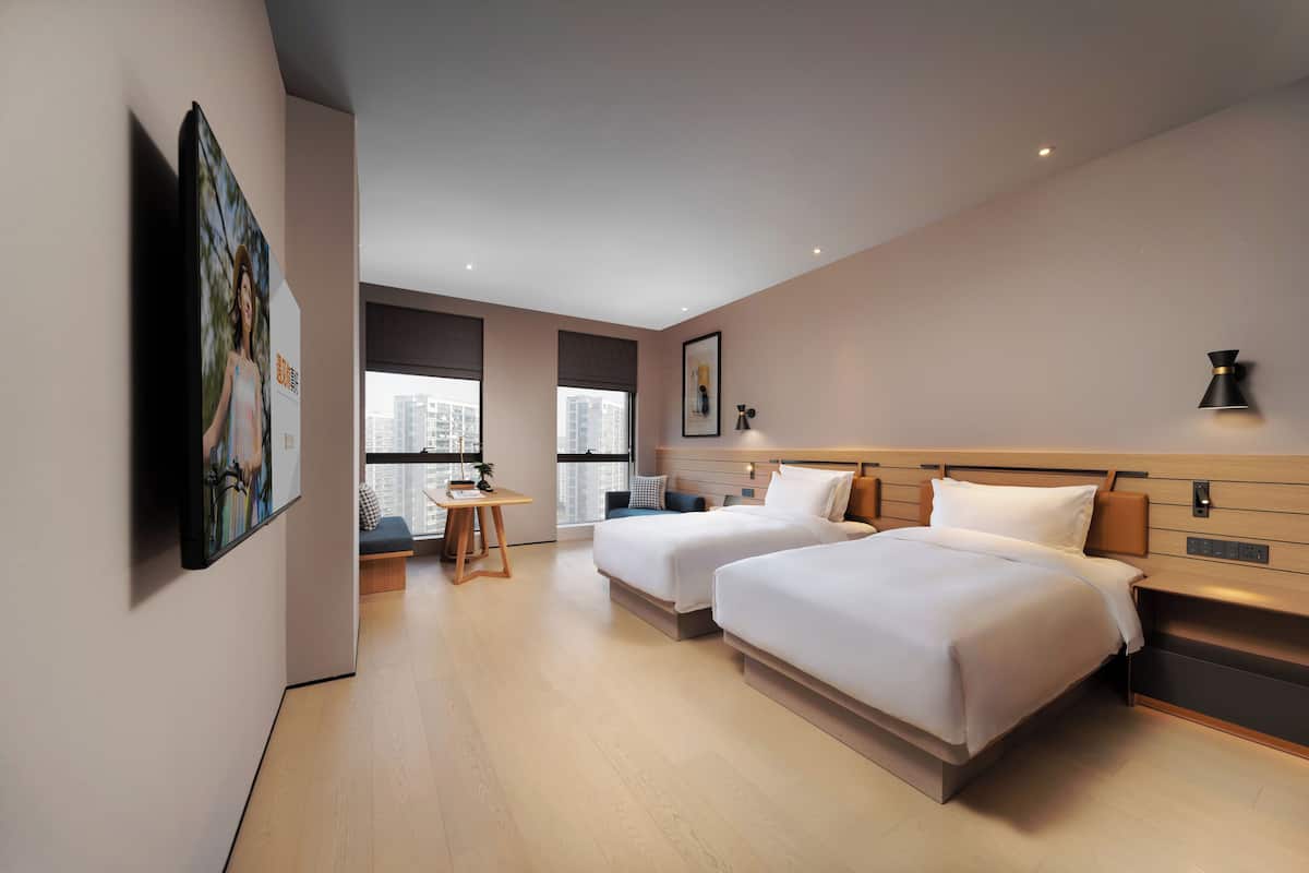 Een moderne hotelkamer met twee bedden, een bureau en uitzicht op de stad.