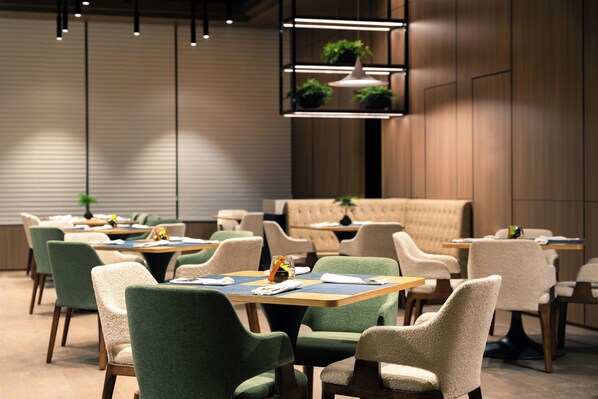 A modern dining area with green and beige upholstered chairs, wooden tables, and pendant lighting. - SSAW Boutique Hotel Hangzhou City University - Near The Grand Canal (Hangzhou)