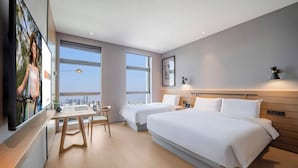 Ein modernes Hotelzimmer mit einem großen Bett, einem Schreibtisch und einem Stuhl. Zwei Fenster bieten Blick auf die Stadt.