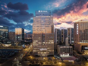 A modern hotel building with a grid-like facade, surrounded by other high-rise buildings and a busy street at dusk. - SSAW Boutique Hotel Hangzhou City University - Near The Grand Canal (Hangzhou)
