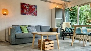 A modern living room with a grey sofa, a wooden coffee table, and a black chair with a patterned cushion. - Modern Bungalow Near Beach, Forest (Sint Maartensvlotbrug)