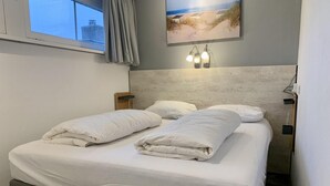 A double bed with white bedding, a headboard, and a wall-mounted light fixture. - Modern Bungalow Near Beach, Forest (Sint Maartensvlotbrug)