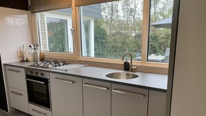 A modern kitchen with a built-in oven, a stainless steel sink, and a window with a view of greenery outside. - Modern Bungalow Near Beach, Forest (Sint Maartensvlotbrug)