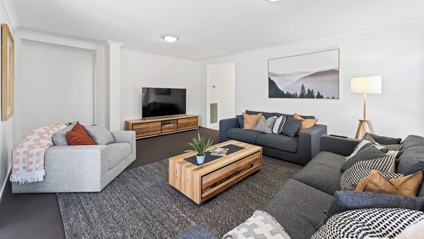A modern living room with a grey sofa, a wooden coffee table, and a TV on a wooden cabinet. - Large stylish home in Bendigo, perfect for families, close to sporting precinct  (Jackass Flat)