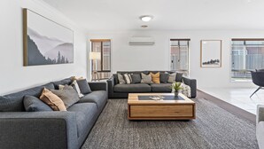 A modern living room with two grey sofas, a wooden coffee table, and a large landscape painting on the wall. - Large stylish home in Bendigo, perfect for families, close to sporting precinct  (Jackass Flat)