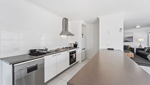 A modern kitchen with white cabinetry, a stainless steel dishwasher, a built-in oven, and a central island with a dark countertop. - Large stylish home in Bendigo, perfect for families, close to sporting precinct  (Jackass Flat)