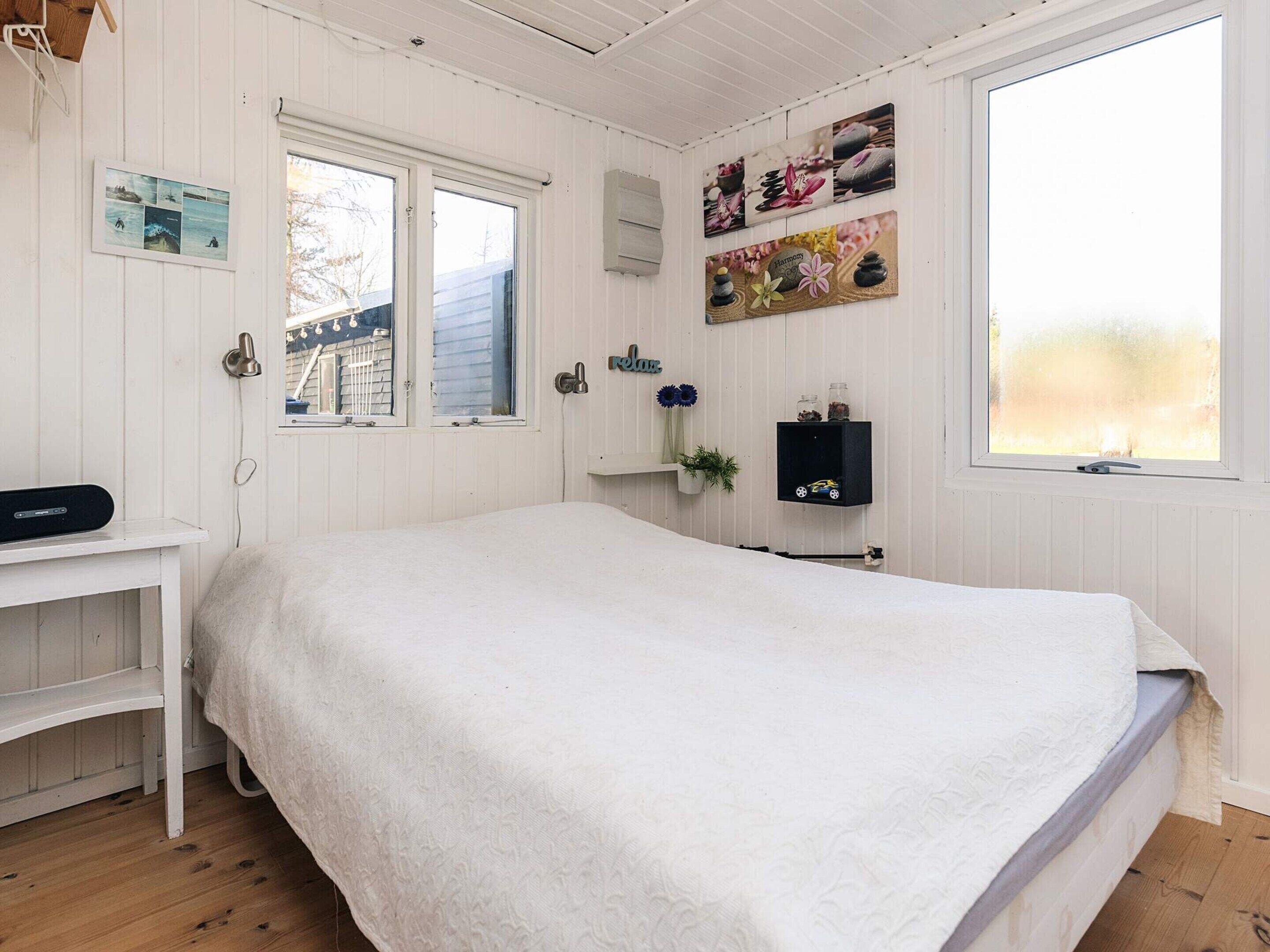 Un dormitorio con una cama grande, un escritorio pequeño, una estantería con objetos decorativos y una ventana con vistas.
