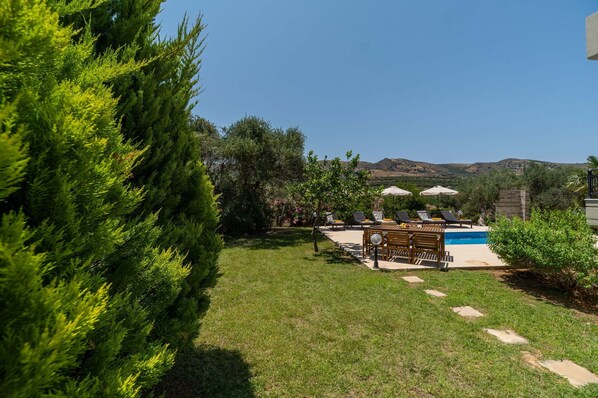 Un jardin avec une piscine, des chaises longues et une table en bois.