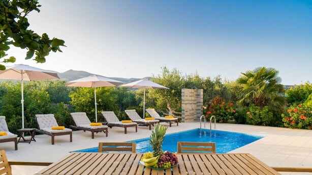 A poolside area with lounge chairs, umbrellas, and a table with fruit.