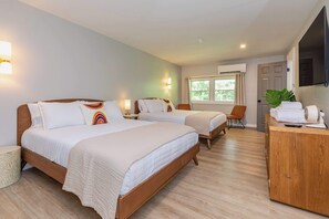 A hotel room with two beds, a wooden dresser, a TV, and a window with curtains.