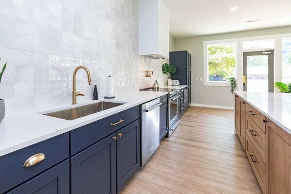 A modern kitchen with dark cabinets, a white countertop, stainless steel appliances, and a large window providing natural light.