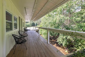 A covered porch with a wooden floor, metal chairs, and a railing overlooking a wooded area. - Maple Deluxe Double Queen Suite at The Dogwood (Maggie Valley)