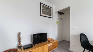 Una sala moderna con un televisor de pantalla plana sobre un mueble de madera, un cuadro en la pared y una silla negra.