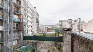 Un edificio residencial de varios pisos con balcones, techo verde y un patio con plantas en macetas.