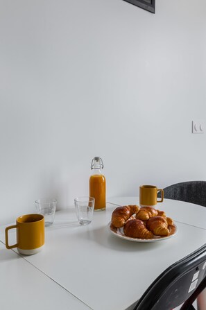 A white table with a plate of croissants, a glass bottle, and two yellow mugs.