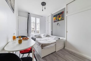 A compact room with a bed, a small table with breakfast items, a window with curtains, and a wall-mounted artwork. - Studio Cosy proche tour Eiffel - Paris 7 - 2P (Paris)