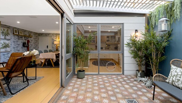 Ein modernes Interieur mit einem Essbereich, einer durch Glastüren einsehbarer Küche und einem gemusterten Außenboden.