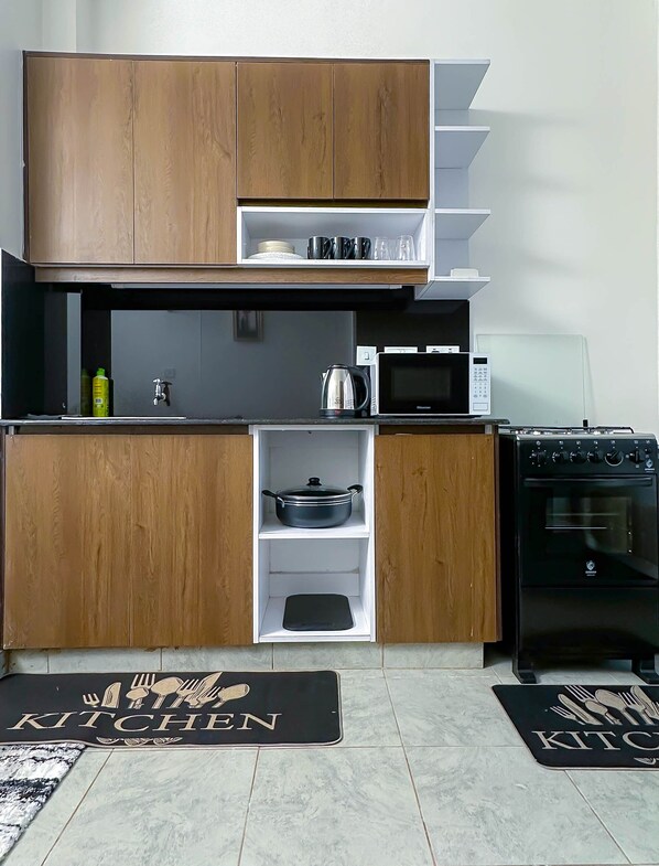 Une cuisine compacte dotée de meubles en bois, d’un four à micro-ondes, d’une bouilloire et d’une cuisinière.