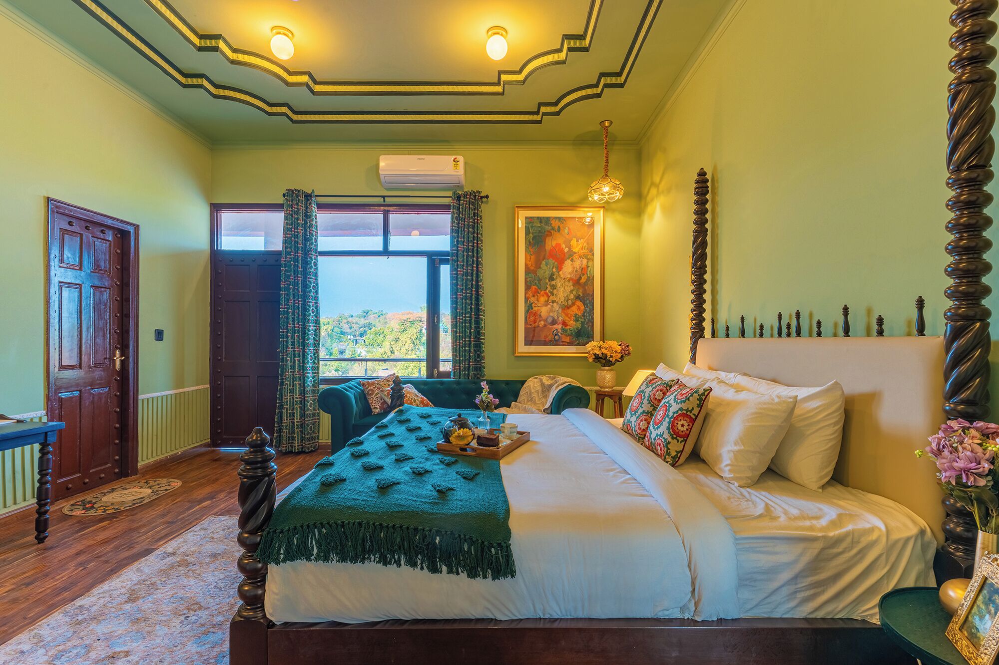 A bedroom with a large bed, a window with curtains, a painting on the wall, and a chandelier.