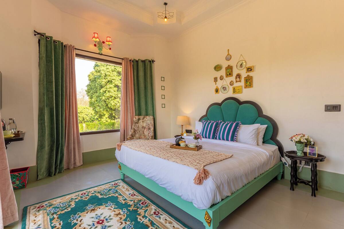 A bedroom with a bed, a bedside table, a nightstand, a window with curtains, and a wall with framed pictures.