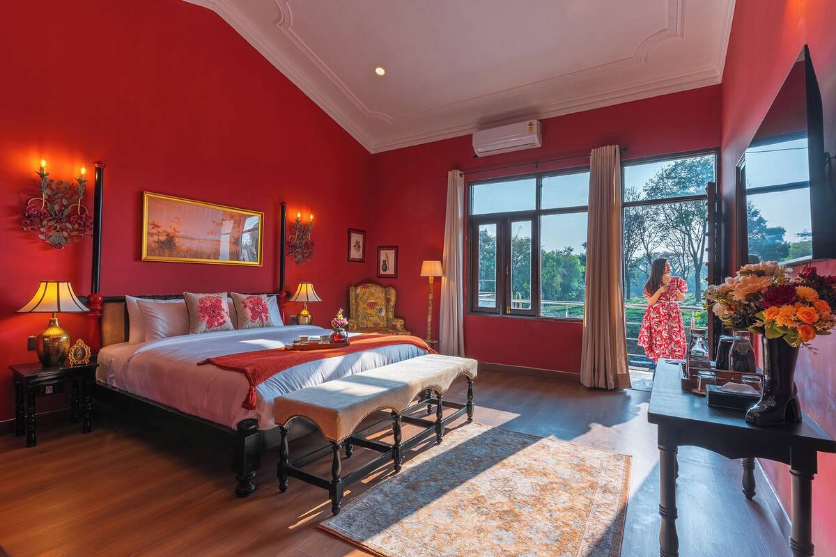 A bedroom with a large bed, a desk with a vase of flowers, and a view of the outdoors through the window.