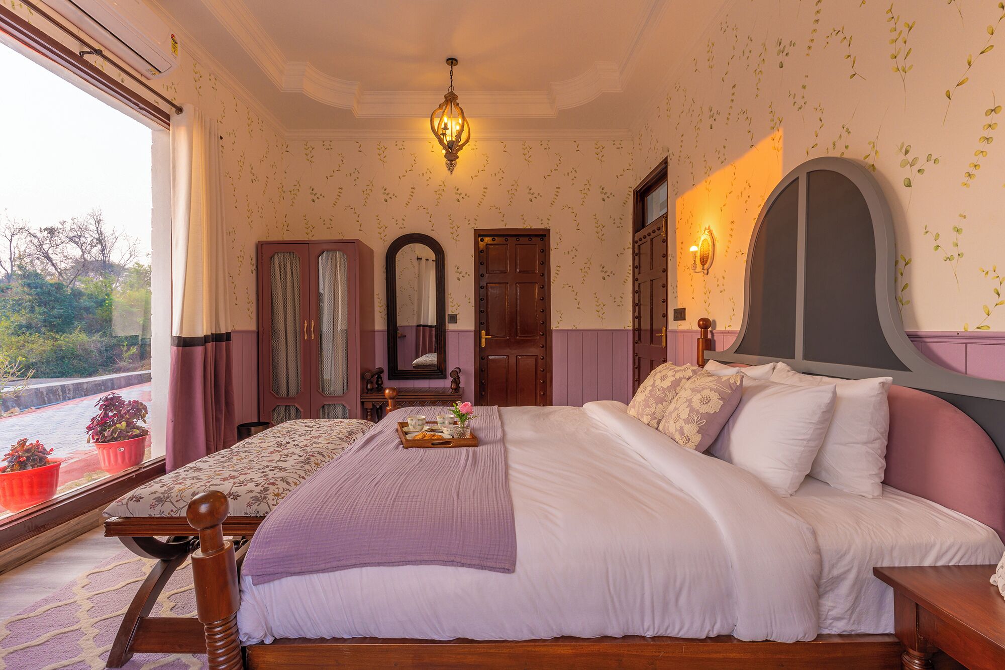A bedroom with a large bed, a wooden headboard, a dresser, a mirror, and a window with a view of greenery.