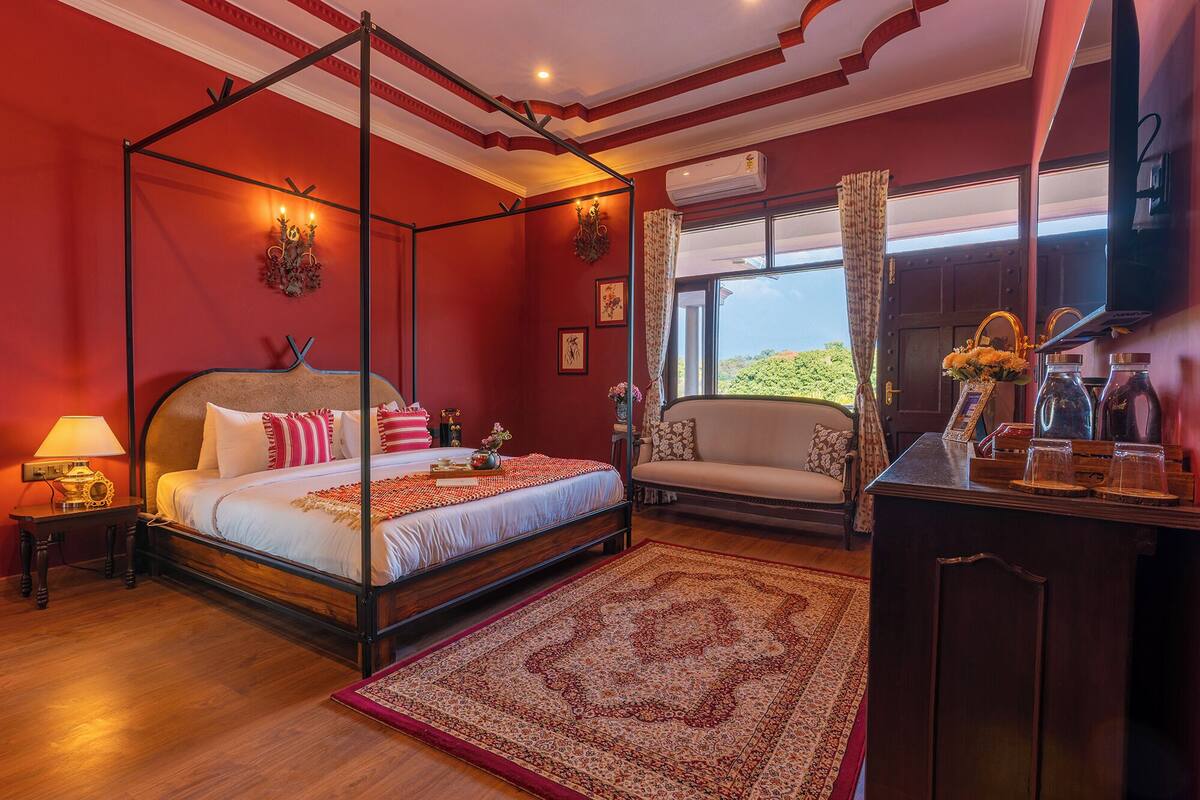 A four-poster bed with a canopy, a sofa, a wooden cabinet, and a large window with curtains.