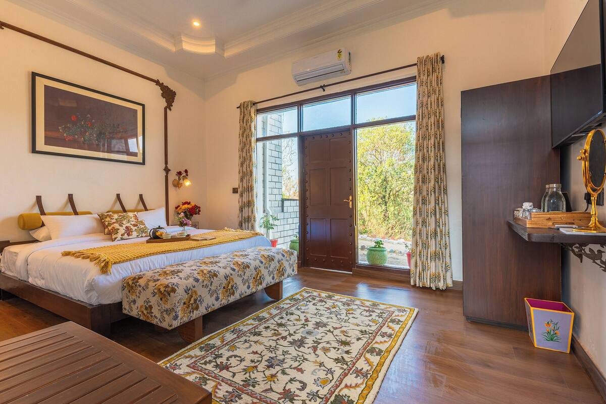 A bedroom with a large bed, a wooden desk, a mirror, and a window with curtains.
