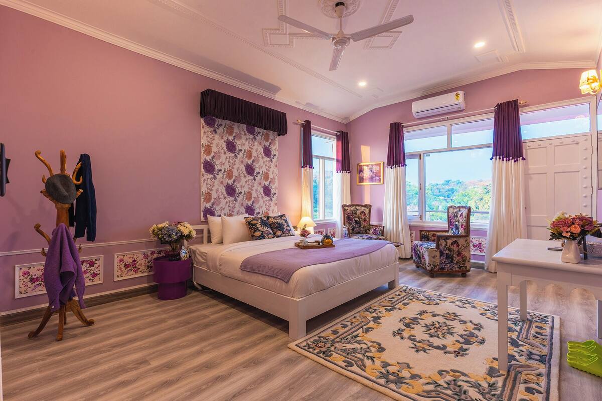 A bedroom with a bed, a chair, a table, and a window with curtains.