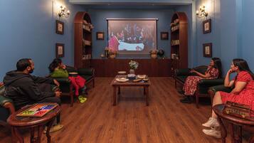 A cozy room with a wooden floor, a central coffee table, and a large screen displaying a movie.