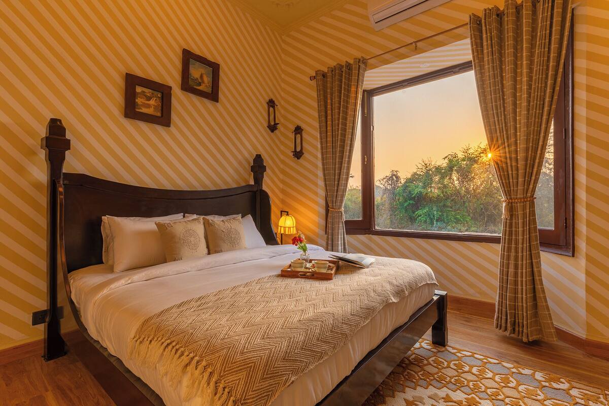A neatly made bed with a wooden headboard, a bedside table with a lamp, and a window with curtains.