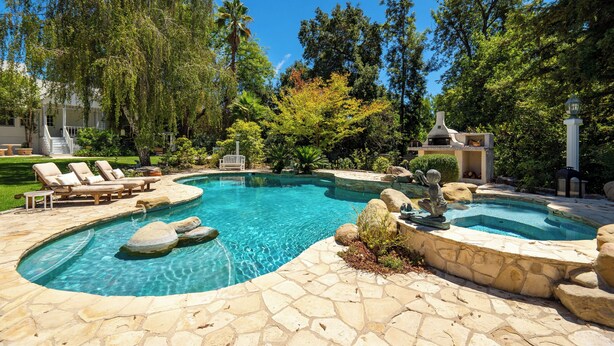 Une piscine entourée d’une terrasse en pierre, avec des chaises longues et un jacuzzi.