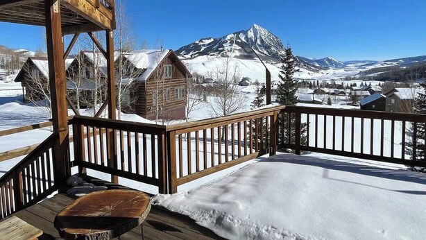 A wooden deck with a view of snow-covered mountains and houses.