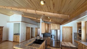 A spacious kitchen with wooden cabinets, a central island, a stainless steel refrigerator, and a dining table.