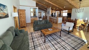 A spacious living area with a wooden ceiling, a sofa, a coffee table, and a dining area with wooden chairs and a table.