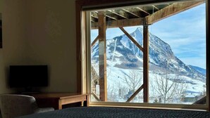 A room with a large window, a bed, a television, and a wooden structure.