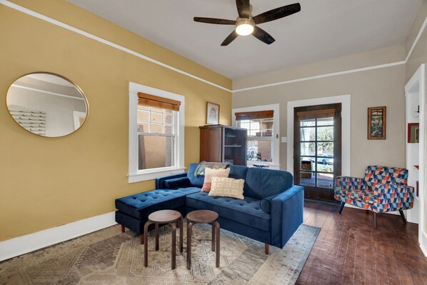 A living room with a blue sectional sofa, two small stools, a ceiling fan, and a patterned rug. - Historic Adobe off 4th Ave, near the U, private yard, Dogs OK! (Tucson)