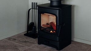 Un poêle à bois moderne, doté d’une haute cheminée noire, avec un feu qui crépite à l’intérieur et un collecteur de cendres noir placé à côté.