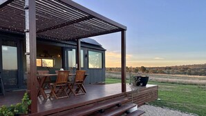 Une terrasse en bois avec des sièges extérieurs, une pergola et une vue sur un champ.