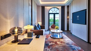 A modern hotel room with a large TV, a sofa, a coffee table, and a view of the outdoors through a large window. - TUI BLUE Taicang Hotel (Suzhou)