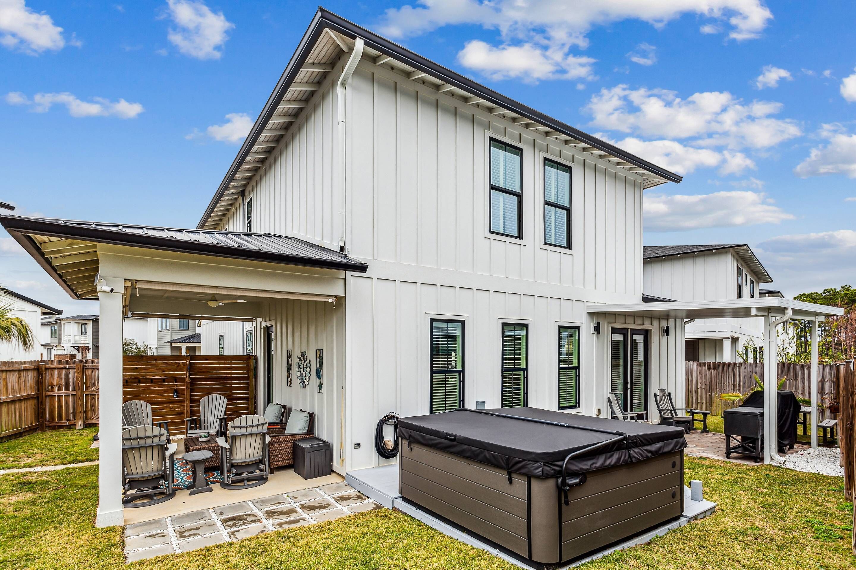 A two-story house with a covered patio area, a hot tub, and a fenced backyard.